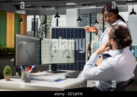 Manager bespricht Solarzellen mit reduzierten CO2-Emissionen mit einem Ingenieur. Teamleiter und Mitarbeiter entwickeln Roboterarmsysteme für die automatisierte Produktion von Solarpaneelen mit sauberer Energie Stockfoto