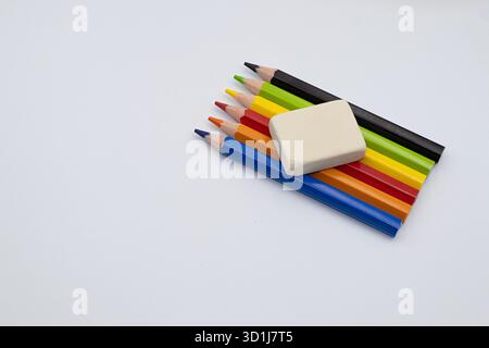 Kunstgegenstände, darunter Buntstifte und ein Radiergummi, auf einer sauberen weißen Oberfläche angeordnet, repräsentieren Kreativität und Bildung Stockfoto