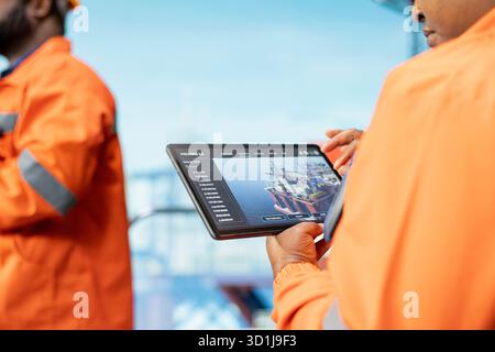 Nahaufnahme von Experten für Offshore-Plattformen, die die Leistung von Geräten in Echtzeit über eine Tablet-App überwachen. Bohrgerätekollegen arbeiten zusammen, um das Getriebe mit dem Asset Management System am Gerät zu kalibrieren Stockfoto
