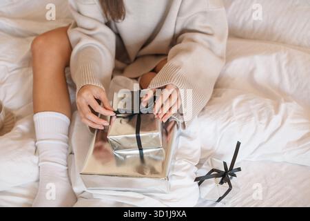 Nahaufnahme einer jungen Frau, die auf einem Bett sitzt mit eingewickelten Weihnachtsgeschenken Stockfoto