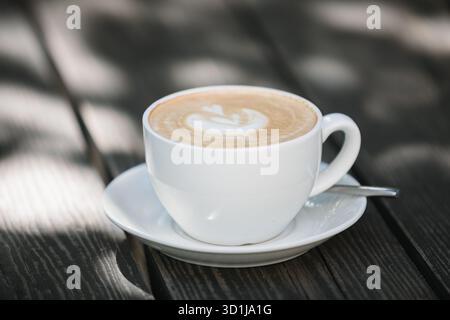 Nahaufnahme eines Latte Coffee auf einem hölzernen Gartentisch im Sonnenlicht Stockfoto