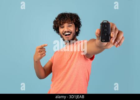Fröhlicher junger Mann, der sich auf den neuen Autoschlüssel vor blauem Hintergrund freut Stockfoto