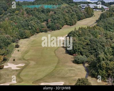 Ein Golfplatz mit einem grünen, grasbewachsenen Hügel und einem Pfad. Der Weg ist von Bäumen umgeben und es gibt ein paar Leute auf dem Platz Stockfoto