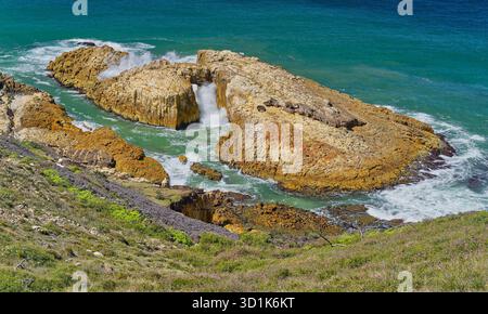 Die Wellen brechen am sonnigen Tag auf der Diamond Head Wanderung in Crowdy Bay, New South Wales, Australien, durch den natürlichen Meeresbogen in Felsformation Stockfoto
