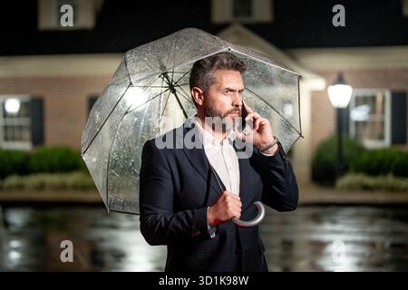 Nachtgeschäft. Geschäftsmann redet in einer regnerischen Nacht unter einem Schirm am Telefon. Der Manager macht im Regen einen Geschäftsanruf. Handytelefon für Mann in Anzug Stockfoto