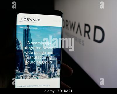In dieser Abbildung hält eine Person ein Mobiltelefon mit der Webseite des US-amerikanischen Designunternehmens Forward Industries Inc. Vor dem Logo. Stockfoto