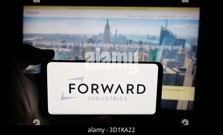 In dieser Abbildung hält eine Person ein Mobiltelefon mit dem Logo des US-amerikanischen Designunternehmens Forward Industries Inc. Auf dem Bildschirm vor der Webseite. Stockfoto