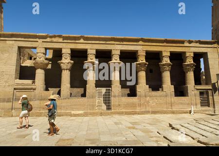 Touristen, die in der Nähe eines antiken Steintempels mit geschnitzten Säulen unter einer historischen archäologischen Stätte spazieren, Philae Tempelkomplex, Assuan, Ägypten Stockfoto
