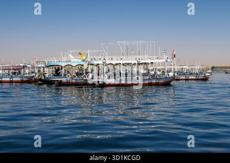 Bootstouren mit bunten Baldachinen, die auf ruhigem blauem Wasser unter klarem Himmel am Nil in Ägypten angedockt sind Stockfoto
