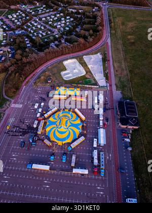 Aus der Vogelperspektive des pulsierenden Zirkus auf dem Parkplatz, blau-gelbes Spiralzelt umgeben von Anhängern und kleineren Zelten Stockfoto