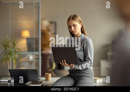 Junge Erwachsene Kaukasierin, die im Büro auf dem Schreibtisch sitzt Stockfoto