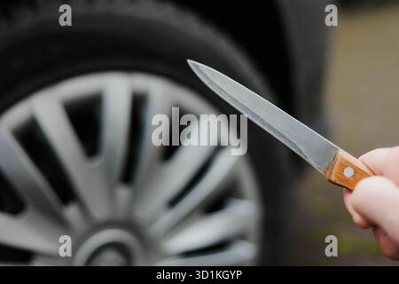 Nahaufnahme einer Frau hält ein Messer in der Hand nahe einem Autorad. In einen Autoreifen schneiden. Stockfoto