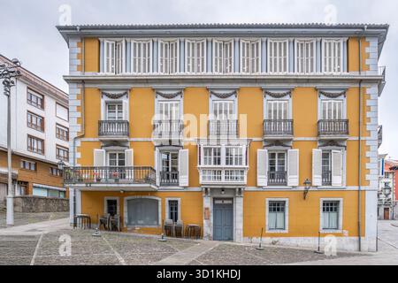 Symmetrische gelbe Wohnfassade mit weißen Holzläden und schmiedeeisernen Balkonen auf einem baskischen Küstenplatz Stockfoto