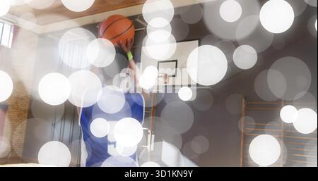 Hüpfender männlicher Basketballspieler mit blauem Trikot Nummer 5, der im Fitnessstudio den Ball hält, mit einem Korb Stockfoto