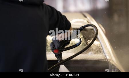 Professioneller Mitarbeiter, der ein Auto mit einer Hochdruckspritze bei einem Autodetailservice reinigt. Nahaufnahme des Waschvorgangs mit Schaum und Wasser, Rep Stockfoto