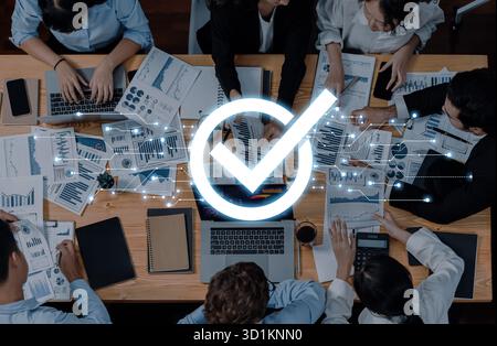 Ein vielseitiges Team arbeitet an einem modernen Bürotisch zusammen und prüft Diagramme und Berichte. Ein leuchtendes Häkchen symbolisiert erfolgreiche Geschäftsstrategien Stockfoto