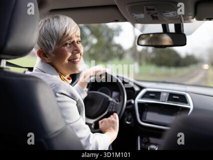 Lächelnde Seniorin sitzt im Auto und blickt zurück über den Sitz Stockfoto