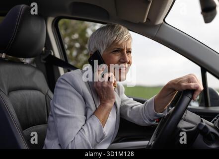 Geschäftsfrau, die versucht, sich auf die Straße zu konzentrieren und aufmerksam Auto zu fahren, während sie telefoniert Stockfoto