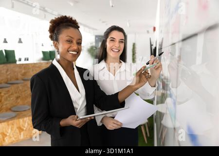 Arbeitsplatzportrait zwei glückliche multiethnische Geschäftsfrauen, die an der Projektplanung arbeiten Stockfoto