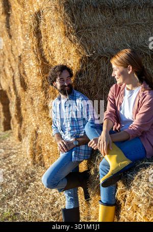 Mann und Frau, die sich auf Heu lehnen und sich nach der harten Arbeit auf dem Feld entspannen Stockfoto