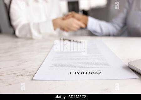 Großaufnahmetapier-Vertrag auf dem Schreibtisch und zwei Geschäftsfrauen, die Hand schütteln Stockfoto