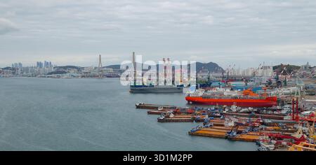 BUSAN, SÜDKOREA - 9. OKTOBER 2025 - Busan Hafen mit verschiedenen Schiffen an einer großen Werft und einer Skyline der Stadt Stockfoto