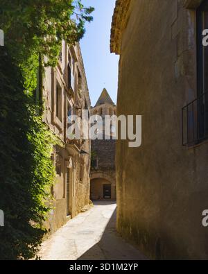 Enge Gasse im historischen ummauerten Zentrum von Madremanya, Katalonien, mit alten Steinhäusern und einem Glockenturm im Hintergrund. Stockfoto