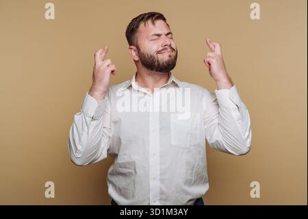 Mann mit Bart, Finger kreuzen und Augen schließen, auf Glück hoffen. Stockfoto