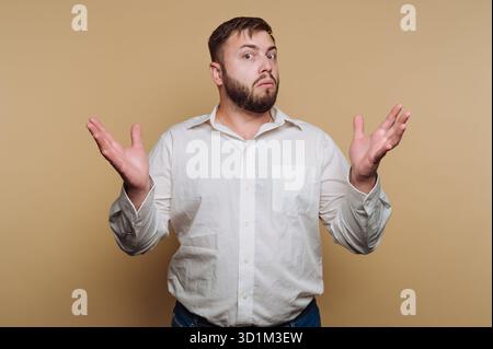 Mann in weißem Hemd mit verwirrtem Ausdruck vor beigefarbenem Hintergrund Stockfoto
