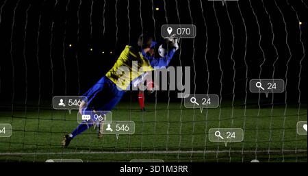 Torhüter in gelb-blauem Trikot taucht auf dem Nachtfeld mit digitalen Symbolen in Richtung weißem schwarzen Ball Stockfoto