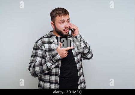 Mann in kariertem Hemd, der telefoniert und seitwärts zeigt Stockfoto