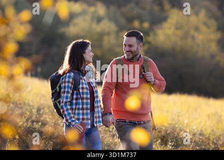 Ein paar Spaziergänge Hand in Hand durch einen sonnigen Herbstpark, umgeben von farbenfrohen Blättern und goldenem Sonnenlicht. Sie teilen Lächeln und Lachen Stockfoto