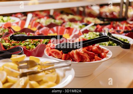 Bunte Schüsseln mit frischem Gemüse, Kräutern und Obst sind ordentlich auf einem Buffet-Tisch angeordnet. Gäste können ihre eigenen Salate mit verschiedenen Zutaten zubereiten Stockfoto