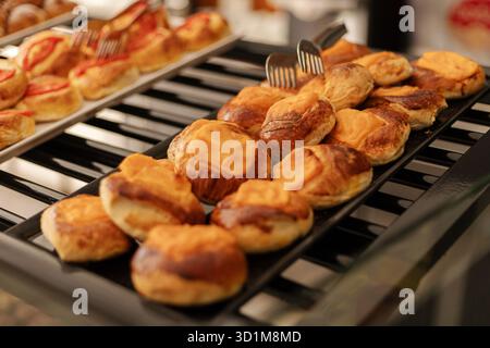 Verschiedene Gebäcksorten, darunter süße und herzhafte Speisen, werden bei einem lebhaften Frühstücksbuffet in einem einladenden Café auf einem schwarzen Tablett ordentlich zubereitet Stockfoto