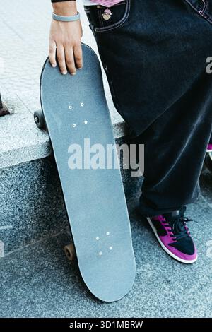 Nahaufnahme eines Skaters ist die Hand, die ein Skateboard hält, während sie auf einer Stadtbank ruht Stockfoto
