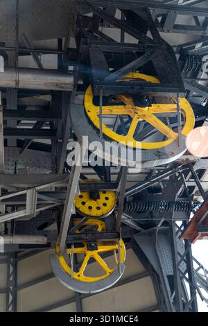 Technische Struktur: Ein System von Riemenscheiben und Kabeln zum Bewegen einer Hubkabine. Alte Industriemechanik, Nahaufnahme eines mehrtonigen gelben Rades Stockfoto