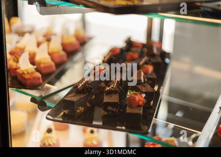 Eine Glasvitrine zeigt verschiedene köstliche Gebäckstücke und Desserts. Brownies mit Obst und bunten Mini-Kuchen, perfekt für die Gäste Stockfoto