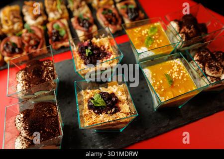 Auswahl an Desserttassen aus Glas, darunter Tiramisu, Chia Pudding mit Mango und mehrschichtige Beerenparfaits auf einem Schiefertablett. Stockfoto