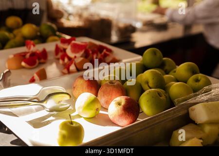 Eine Auswahl an frischem Obst, darunter Äpfel und Grapefruit, werden kunstvoll auf einem Buffettisch arrangiert. Die Umgebung ist hell mit Morgensonne, verbessert Stockfoto