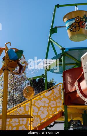 Ein lebendiger Wasserspielbereich bietet farbenfrohe Rutschen und Wasserspiele. Der hellblaue Himmel trägt zur unterhaltsamen Atmosphäre bei und lädt die Kinder ein, das zu genießen Stockfoto