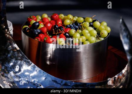 Eine Edelstahlschale gefüllt mit grünen Trauben, schwarzen Trauben, Erdbeeren und Heidelbeeren in natürlichem Licht. Stockfoto