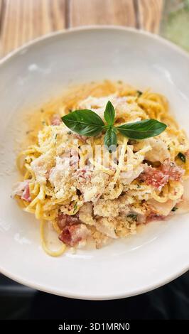 Traditionelles italienisches Pasta-Carbonara-Gericht mit Basilikumblättern auf einem Tisch Stockfoto