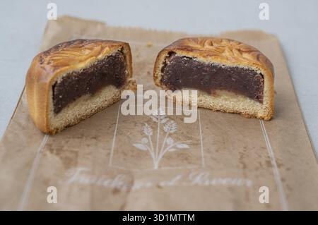 Nahaufnahme eines Mooncake (Mooncake), der in der Mitte mit einer dicken Schicht dunkelroter Bohnenpaste und einer leichten Mürzteigbasis geschnitten ist, präsentiert auf brauner r Stockfoto