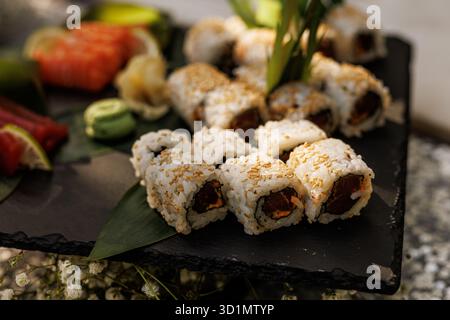Eine Auswahl an Sushi-Brötchen und Nigiri-Stücken ist kunstvoll auf einem hölzernen Servierbrett angeordnet, begleitet von eingelegtem Ingwer und einem Klecks Wasabi. Stockfoto
