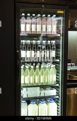 Nahaufnahme eines gekühlten Vitrinenschranks mit bunten Softdrinks und Milch in Glas- und Plastikflaschen auf den Metallregalen Stockfoto