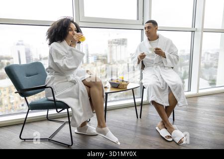 Frühstück. Ein junges Paar in weißen Bademänteln, das frühstückt und glücklich aussieht Stockfoto