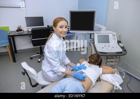 Weibliche Ärztin, die eine Ultraschalluntersuchung der Niere an schulpflichtigen Mädchen-Fachärztin durchführt, die den Rücken des Kindes mit Sonogramm-Geräten im Krankenhaus untersucht Stockfoto