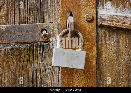Altes, rostiges Vorhängeschloss an Holztüren. Ein veraltetes Schloss hängt an der verwitterten Tür. Rustikale Kulisse Stockfoto