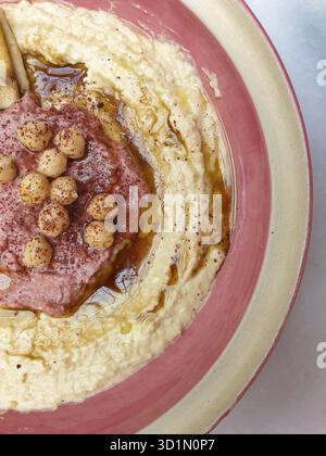 Hummus, arabischer Kichererbsen-Dip, mit Gewürzen auf einem rosa Cremeteller. Abstrakte Erfassung in der Draufsicht. Kopierplatz verfügbar Stockfoto