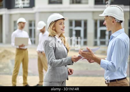 Lächelnde, elegante, kaukasische Vorgesetzte mittleren Alters, die die Mappe mit Dokumenten an einen erfreulichen Vorarbeiter zurückgibt Stockfoto